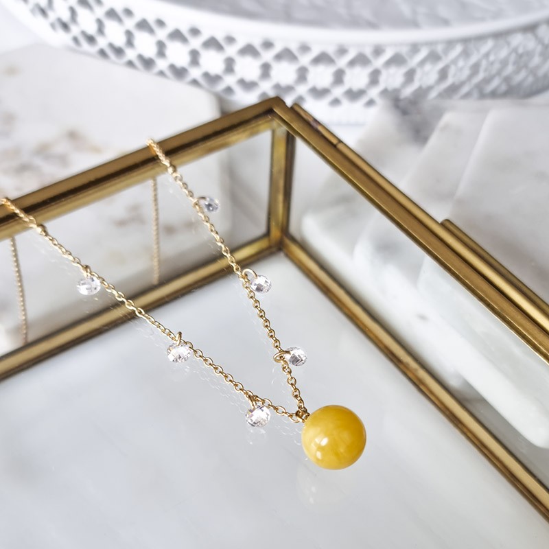 Naszyjnik ze srebra 925 pozłocony 24 karatowym złotem. Ozdobiony cyrkoniami i naturalnym bursztynem w białej barwie.